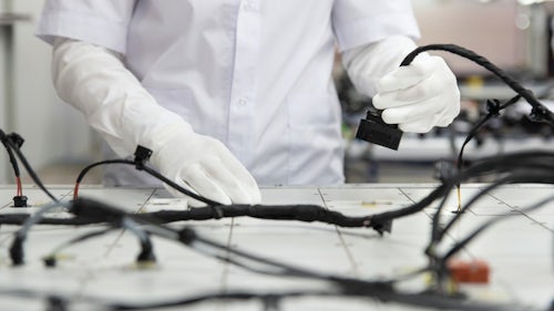 A factory employee working on a complex wire harness on a foamboard.